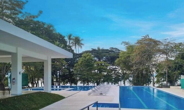 A pool area with a clear sky, trees, and a covered walkway. - Stunning 2 Bedroom Apartment in Punta Esmeralda , Costa Rica (Tárcoles)