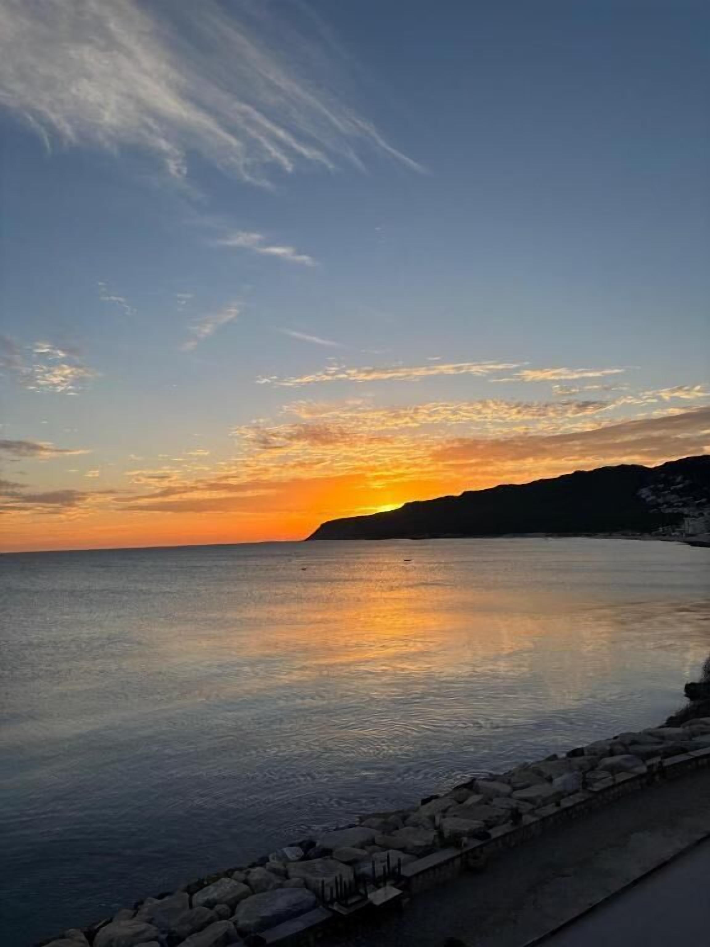 A coastal scene with a calm sea, a stone wall, and a sunset.