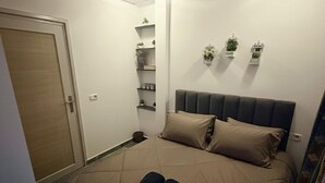 Makuuhuone, jossa on sänky, vaatekaappi, hylly, jossa on kasveja, ja pieni pöytä.