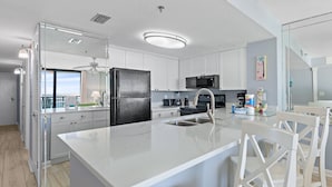 Una cocina moderna con armarios blancos, un refrigerador negro, un microondas y una isla grande con un fregadero.
