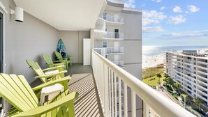 A balcony with green chairs, a small table, and a view of the beach and ocean. - Tradewinds 1106 - Austin Family Retreat (Orange Beach)