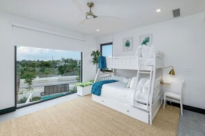 A modern bedroom with a bunk bed, large windows, a ceiling fan, and a view of greenery outside. - Spacious 7-bedroom villa in beautiful Leeward Settlement with AC (Leeward)