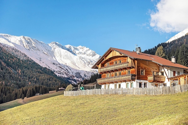 A wooden chalet with a red-tiled roof, wooden balconies, and a view of snow-capped mountains. - Apartment "Burgerhof Firmament" with Mountain View, Shared Terrace and Wi-Fi (Gsies)