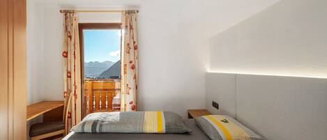 A bedroom with a bed, a desk, and a view of mountains.