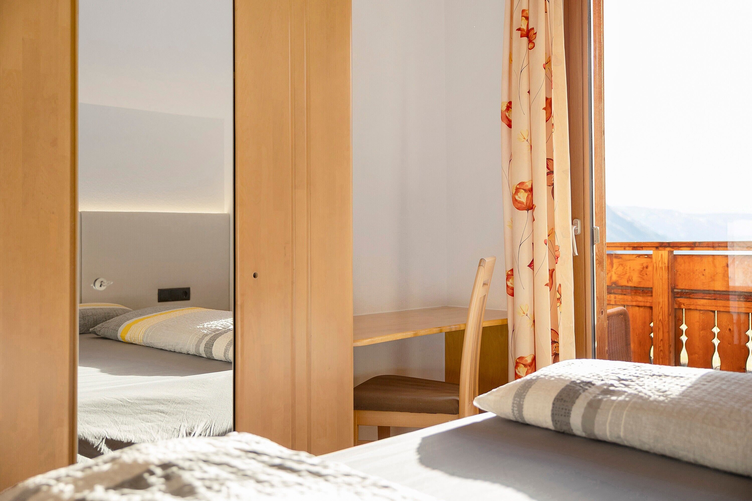 Une chambre à coucher avec un lit, un bureau en bois et une chaise. Il y a une fenêtre avec des rideaux.
