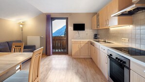 A compact kitchen with wooden cabinets, a built-in oven, and a TV mounted above the counter.