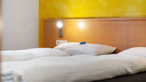 A bed with white bedding, a wooden headboard, and a wall socket.