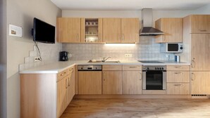 A modern kitchen with wooden cabinets, a dishwasher, an oven, a microwave, and a TV mounted on the wall.