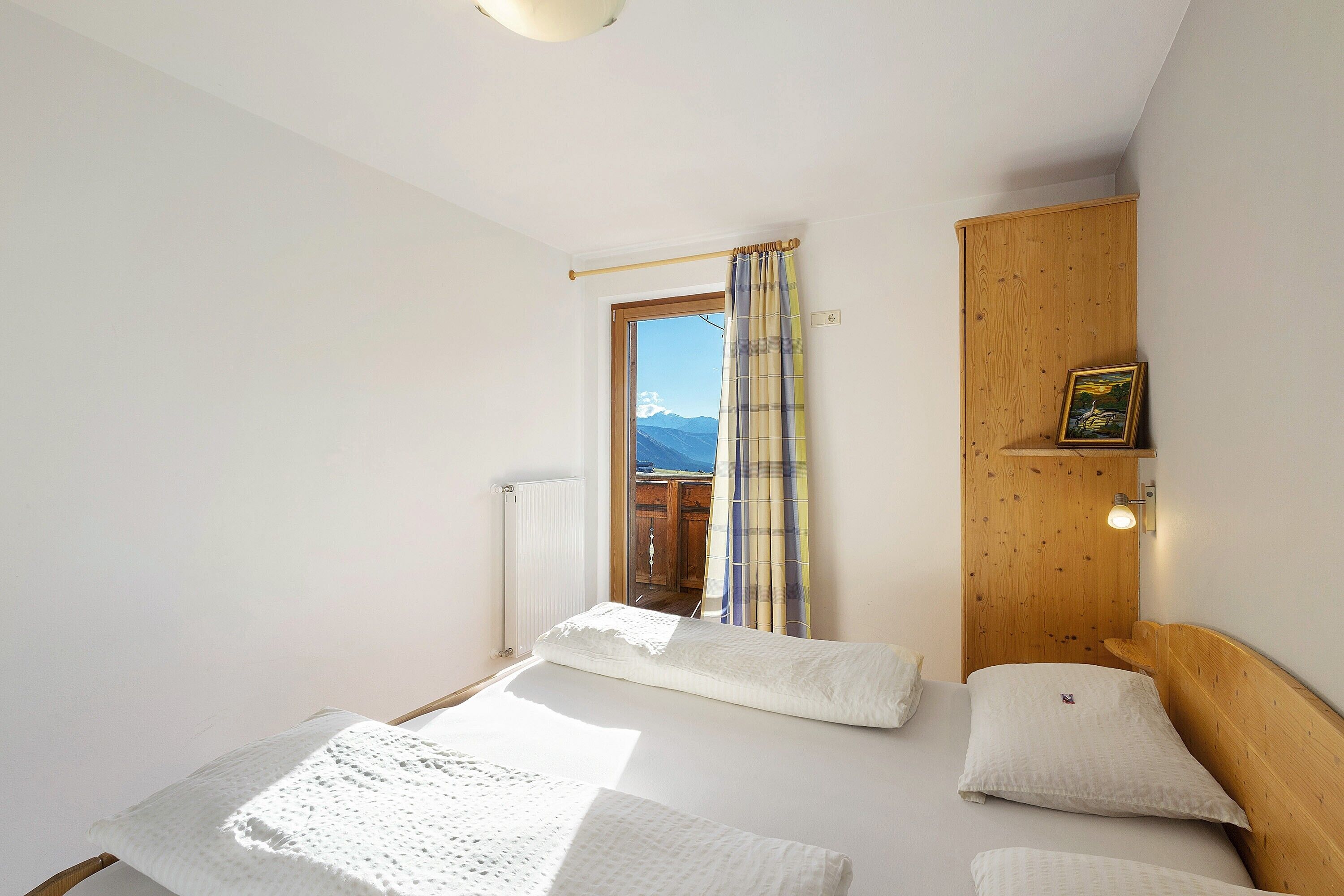A bedroom with a bed, a window with curtains, a wooden headboard, and a wall-mounted light fixture.