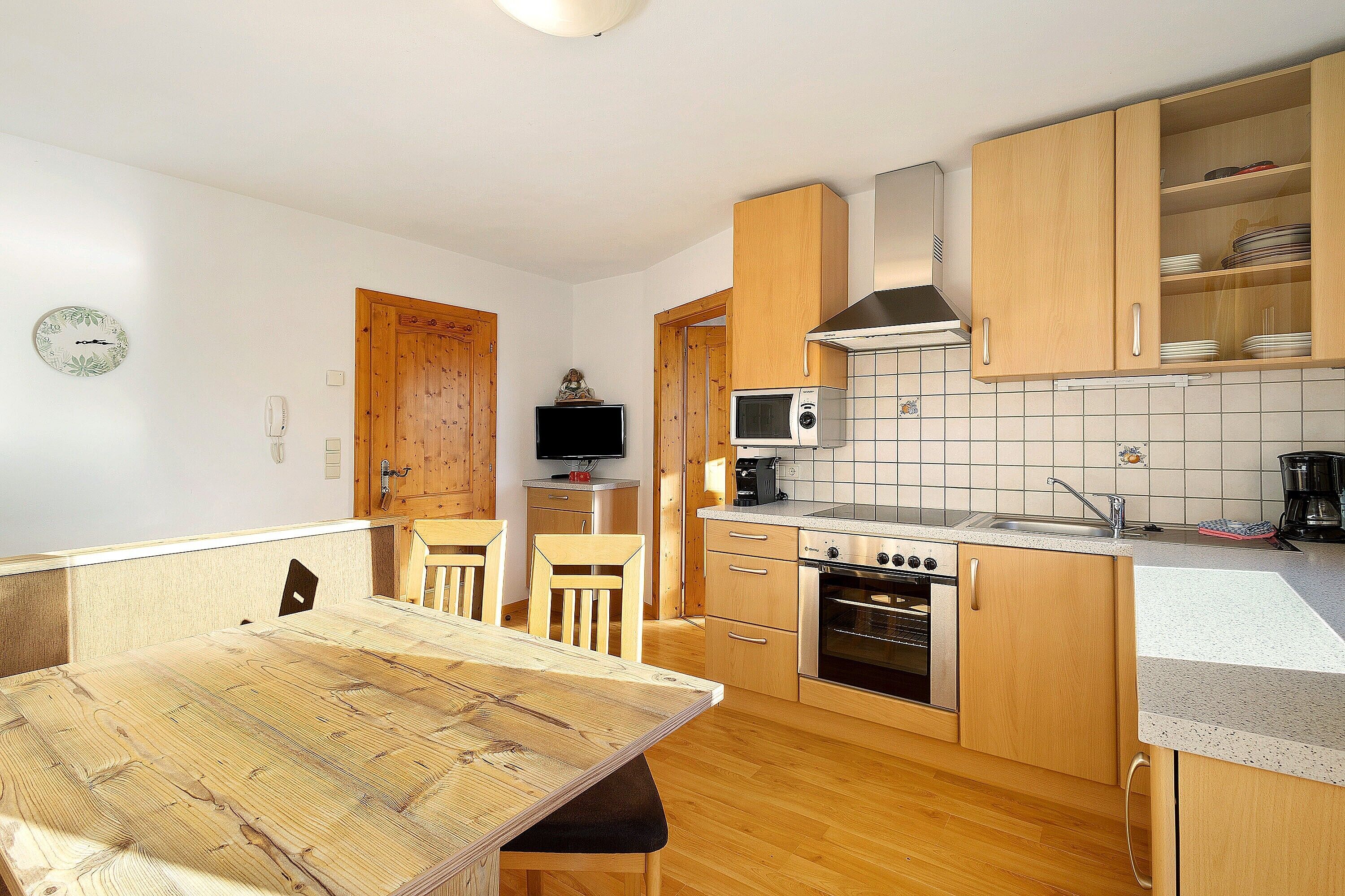 Une cuisine compacte dotée de meubles en bois, d’un four à micro-ondes, d’un four traditionnel et d’un coin repas avec une table et des chaises.