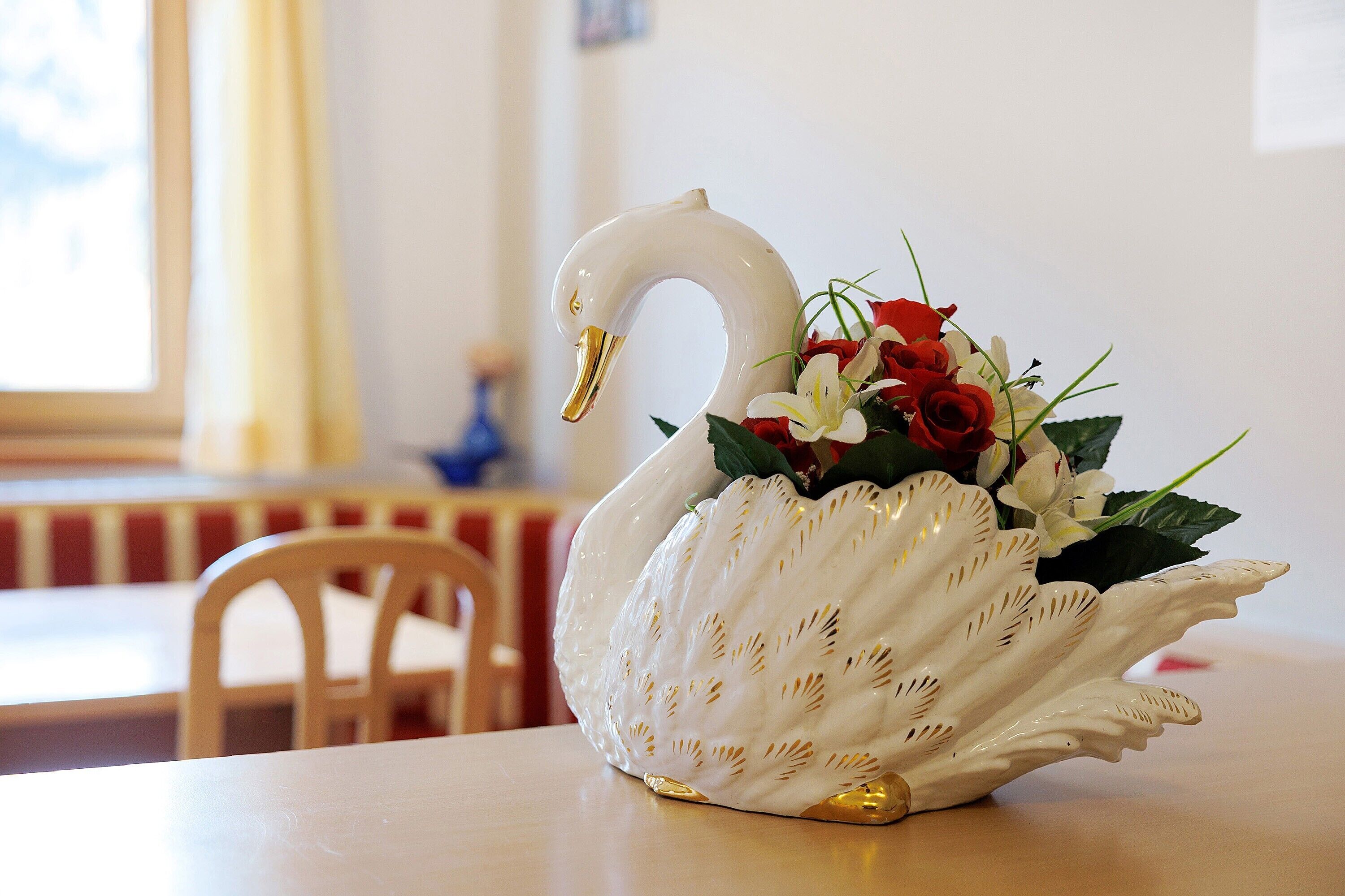 Een witte, zwaanvormige vaas met gouden accenten en een boeket rode en witte bloemen op een tafel.
