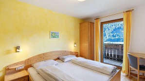 Ein Schlafzimmer mit einem hölzernen Bett, einem Schreibtisch und einem Balkon mit Blick auf Bäume.