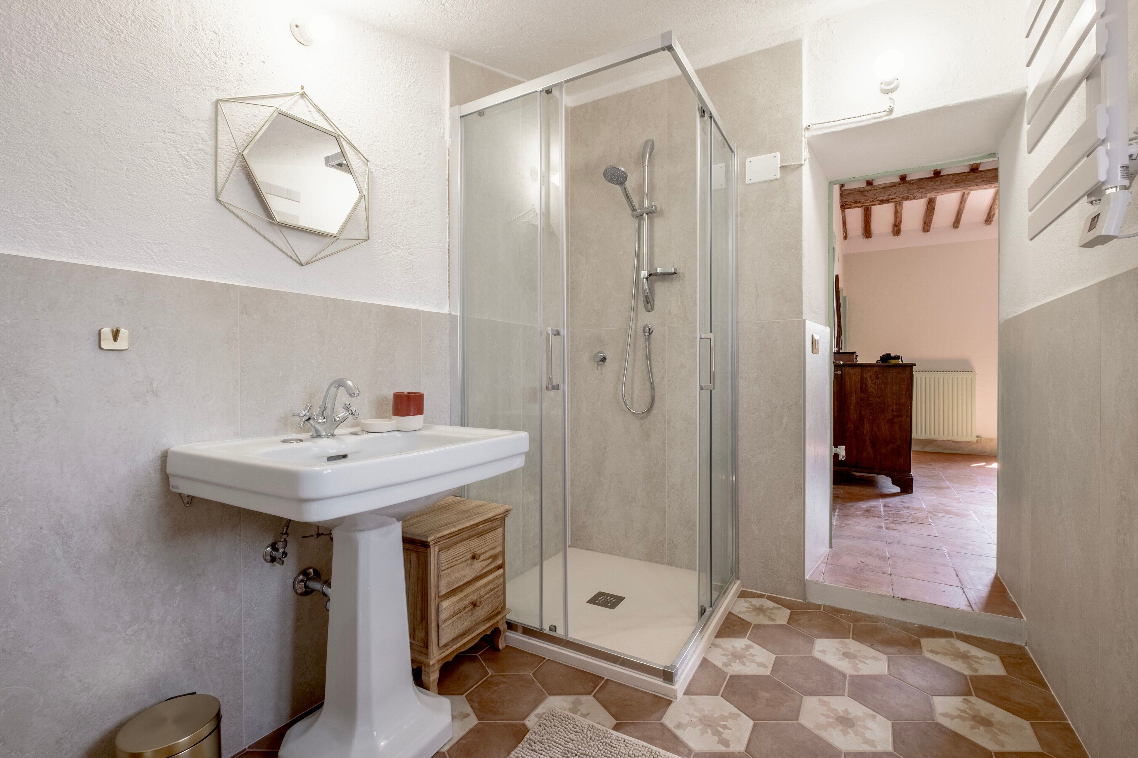 A bathroom with a glass-enclosed shower, a sink, and a mirror on the wall.