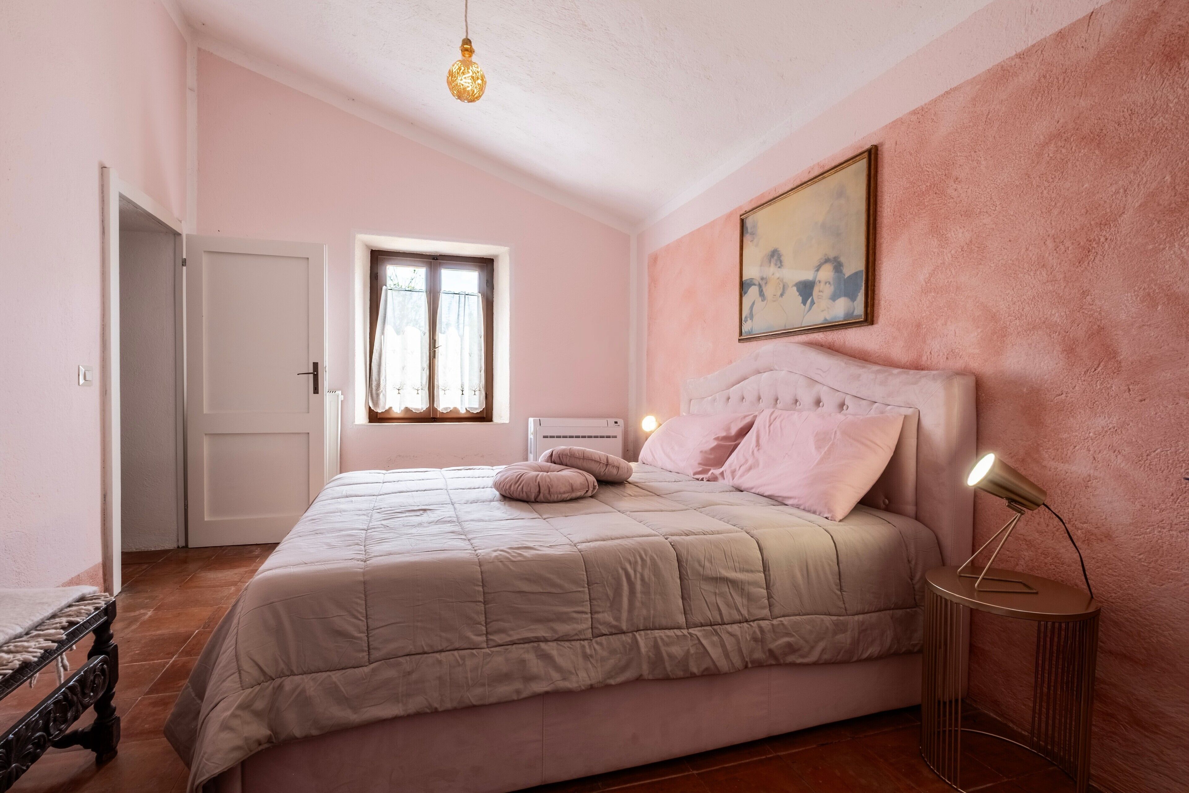 Ein Schlafzimmer mit einem Bett, einer Nachttischlampe, einem Fenster und einem Bild an der Wand.