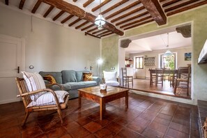 A rustic living room with a wooden coffee table, a wicker chair, a sofa, and a dining area with wooden chairs and a table.
