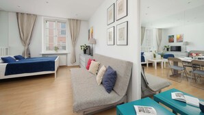 Ein modernes Wohnzimmer mit Sofa, Esstisch und Fernseher. An den Wänden hängen Bilderrahmen und ein Fenster mit Vorhängen.