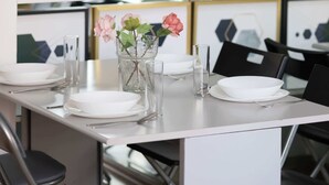 Ein Essbereich mit einem weißen Tisch, gedeckt für vier Personen, einer Blumenvase und Regalen mit Dekoration und Büchern.