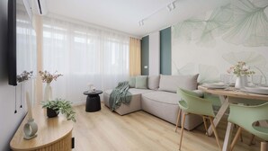Una sala de estar moderna con un sofá seccional, una mesa de comedor con sillas, una mesita auxiliar y un televisor montado en la pared.