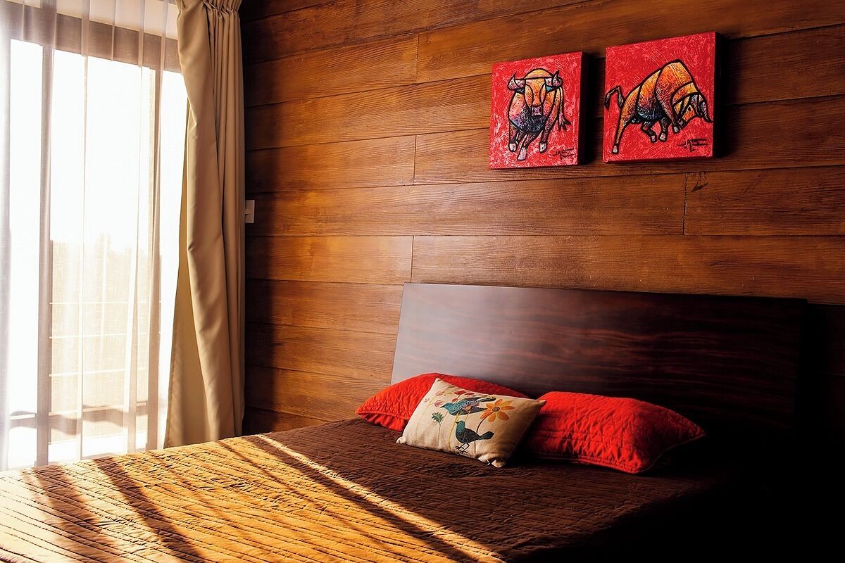 Ein Schlafzimmer mit einem Holz-Kopfteil, einem Bett mit einer braunen Steude und roten Kissen sowie zwei roten Bildern an der Wand.