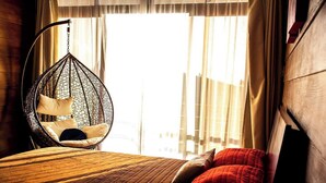 Una habitación con una silla colgante, una cama con colcha y cortinas.