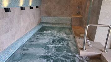 Et spa-område med jacuzzi, flisebeklædte vægge og et bruseområde.