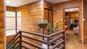 Un interior moderno con paneles de madera, una planta colgante, una escalera y una zona de estar con televisor.
