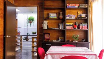 Une pièce avec une bibliothèque en bois, une table à manger entourée de chaises rouges et une vue sur un balcon agrémenté de plantes.