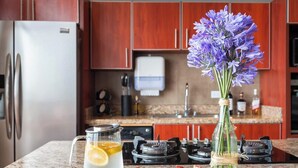 Una cocina con un refrigerador de acero inoxidable, una cafetera, un florero con flores moradas y un plato con rodajas de fruta.