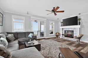 A living room with a sofa, coffee table, fireplace, TV, and ceiling fan. - Bella Shores - Stunning Sunsets & Sandy Shoreline (Coldwater)