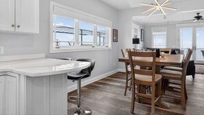 A modern kitchen with a central island, bar stools, and a dining area with wooden chairs. - Lake Days, Bonfires & Endless Memories (Coldwater)