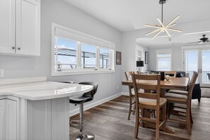 A modern kitchen with a central island, bar stools, and a dining area with wooden chairs. - Bella Shores - Stunning Sunsets & Sandy Shoreline (Coldwater)