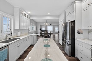 Una cocina moderna con armarios blancos, encimera de mármol y refrigerador de acero inoxidable.