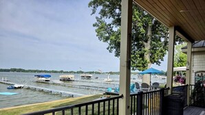 A covered deck with a view of a marina, outdoor seating, and a building with a covered patio. - Lake Days, Bonfires & Endless Memories (Coldwater)