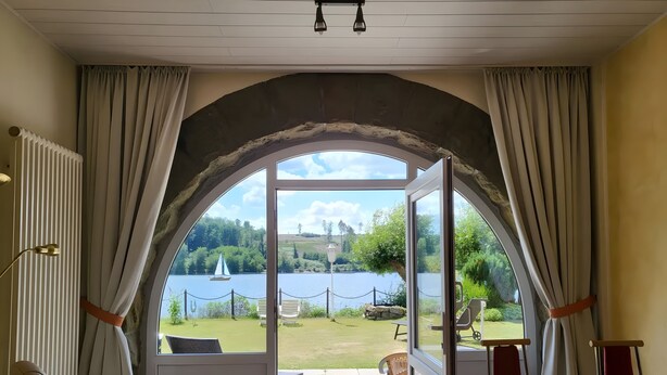 Una stanza con un'ampia finestra ad arco, vista su un lago, area salotto esterna e un tavolo.