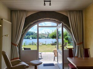 Une pièce dotée d’une grande fenêtre en arc de cercle, offrant une vue sur un lac, avec un espace salon extérieur et une table.