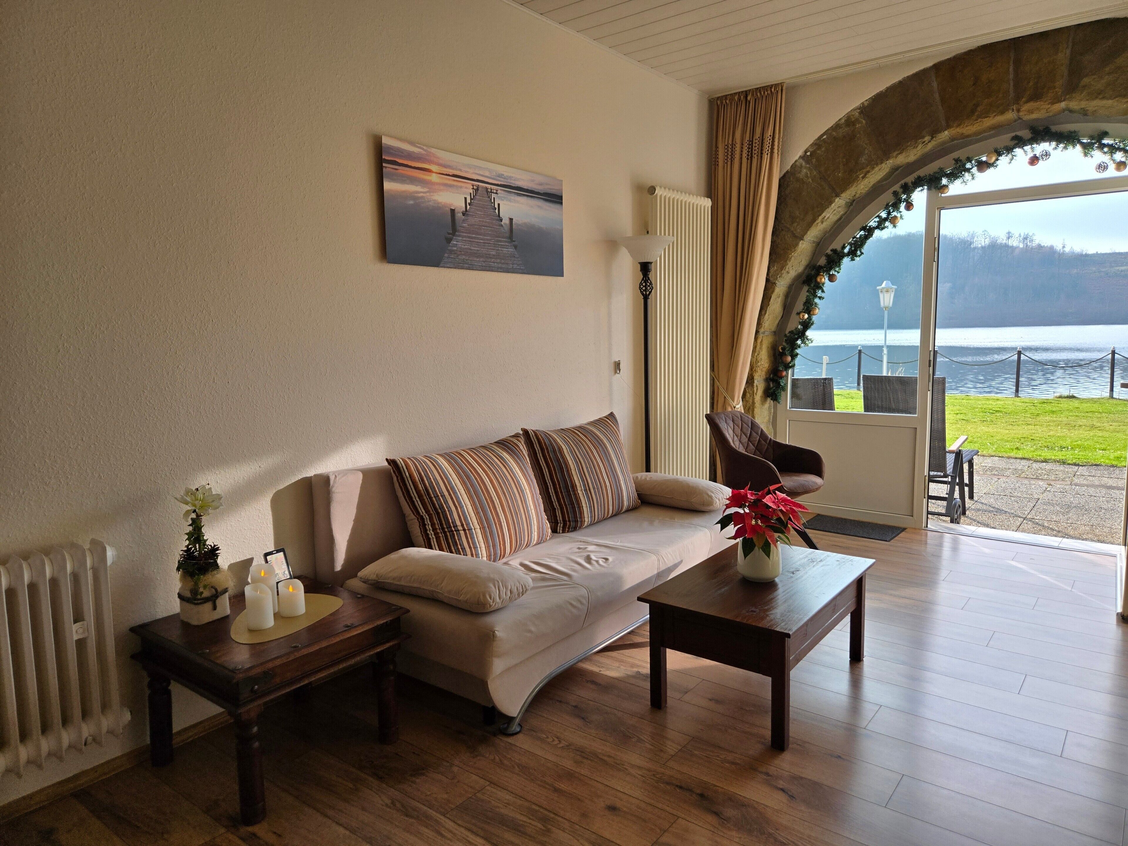 Un salon comprenant un canapé, une table basse, une lampe, un radiateur et une vue sur un lac, visible à travers une fenêtre en arc de cercle.