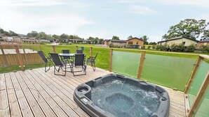Ein Whirlpool auf einer Holterrasse mit Tisch und Stühlen, umgeben von einer grünen Rasenfläche und Häusern im Hintergrund.