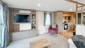 Ein modernes Wohnzimmer mit Flachbildfernseher, einem roten Sessel, einem Holztisch und einer Küchenzeile mit Holdekor und einer Mikrowelle.