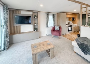 A modern living room with a flat-screen TV, a red armchair, a wooden coffee table, and a kitchen area with wooden cabinets and a microwave. - 1 bedroom accommodation in Eaton, Congleton (Eaton, Congleton)