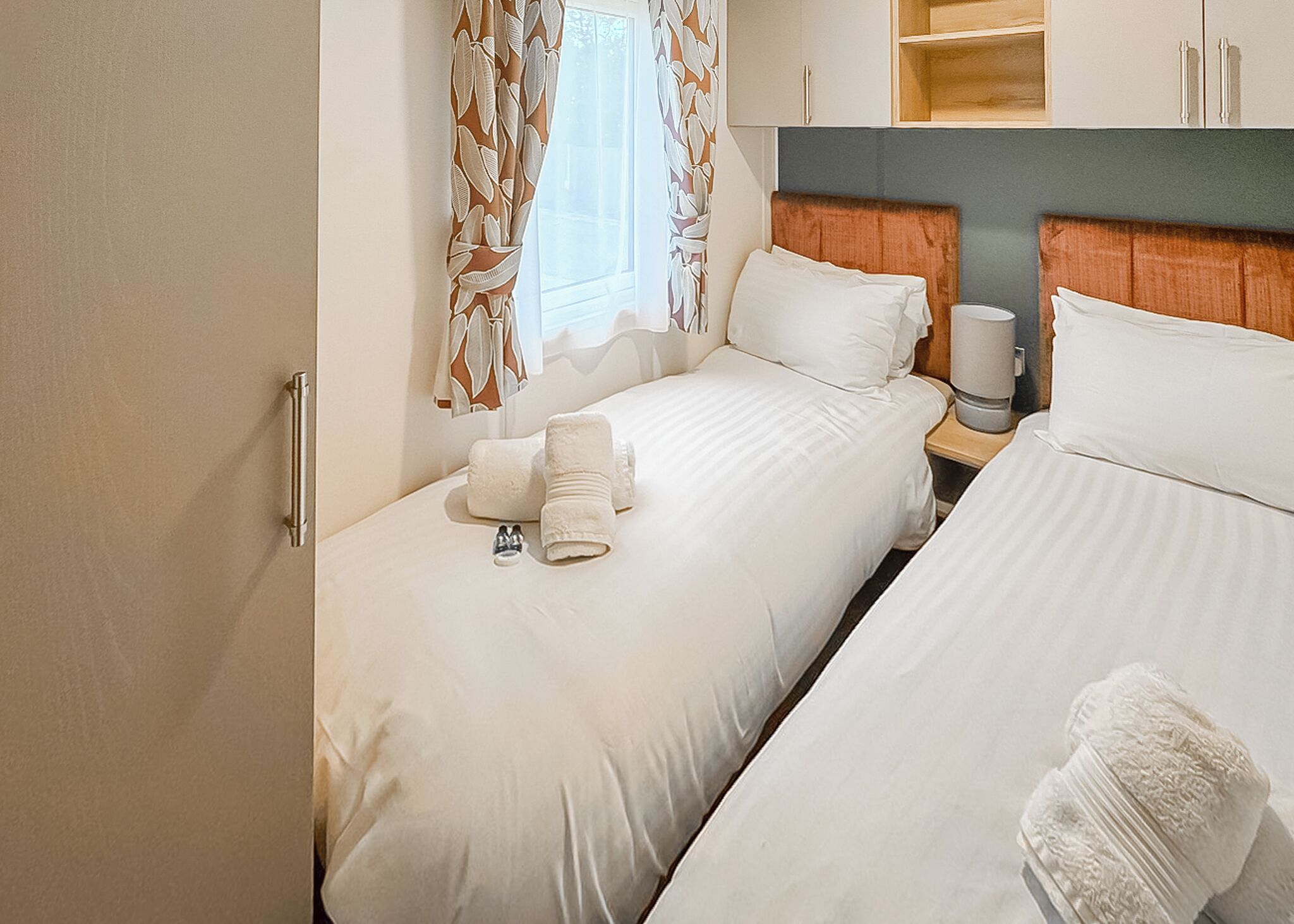 A hotel room with two beds, a nightstand, a window with curtains, and a wooden headboard.