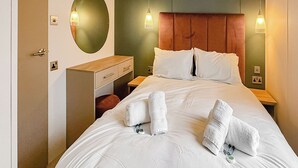 Ein Hotelzimmer mit einem großen Bett, einem Nachttisch aus Holz, einer Kommode und einem runden Spiegel.