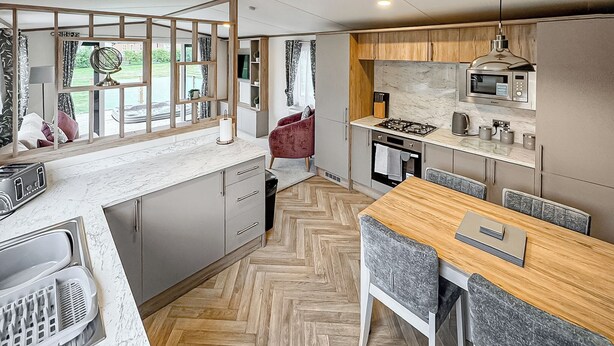 Eine moderne Küche mit Fischgrätparkett, einem Essbereich mit Holztisch und Blick durch ein Fenster.