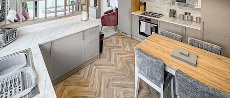 Una cocina moderna con piso de espiga, un comedor con mesa de madera, y vista a través de una ventana.