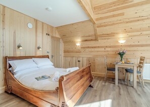A wooden-paneled room with a bed, a table with chairs, and wall-mounted lights.