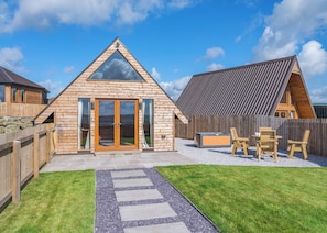 A wooden cabin with a triangular roof, a glass door entrance, and a patio area with outdoor seating.