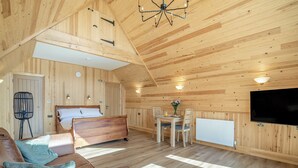 A wooden cabin interior with a bed, sofa, dining table, chairs, a TV, and a radiator. - 1 bedroom accommodation in Ripponden (Ripponden)