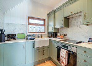 A kitchen with light green cabinets, a marble countertop, a built-in oven, and a window above the sink.