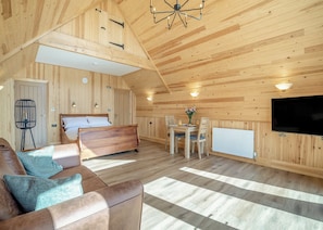 Ein Holzblockhaus-Interieur mit Bett, Sofa, Esstisch, Stühlen, einem Fernseher und einer Heizung.
