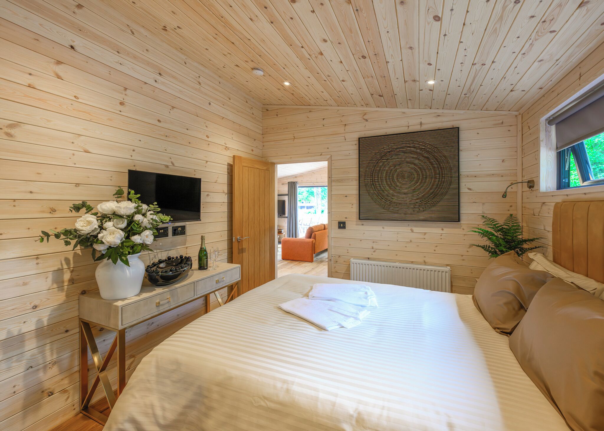 A wooden-paneled bedroom with a bed, a TV, a vase with flowers, and a window.