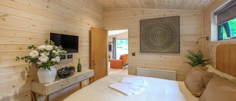 Un dormitorio con paneles de madera, una cama, un televisor, un jarrón con flores y una ventana.